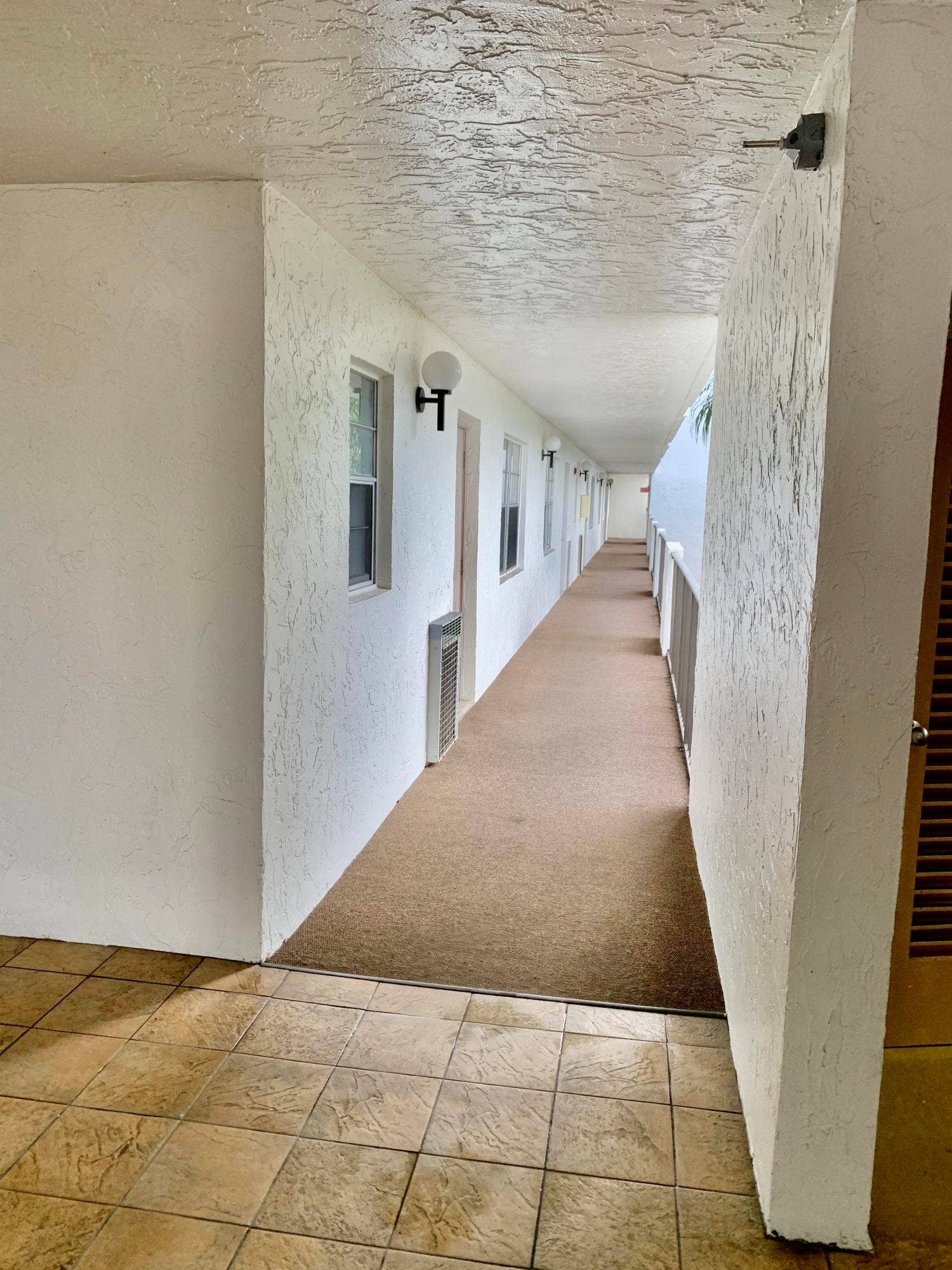 3100 W Rolling Hills Circle, #309, Davie, Davie, FL 33328 Covered exterior walkway featuring textured wall finishes, sconce lighting fixtures, and a carpeted path