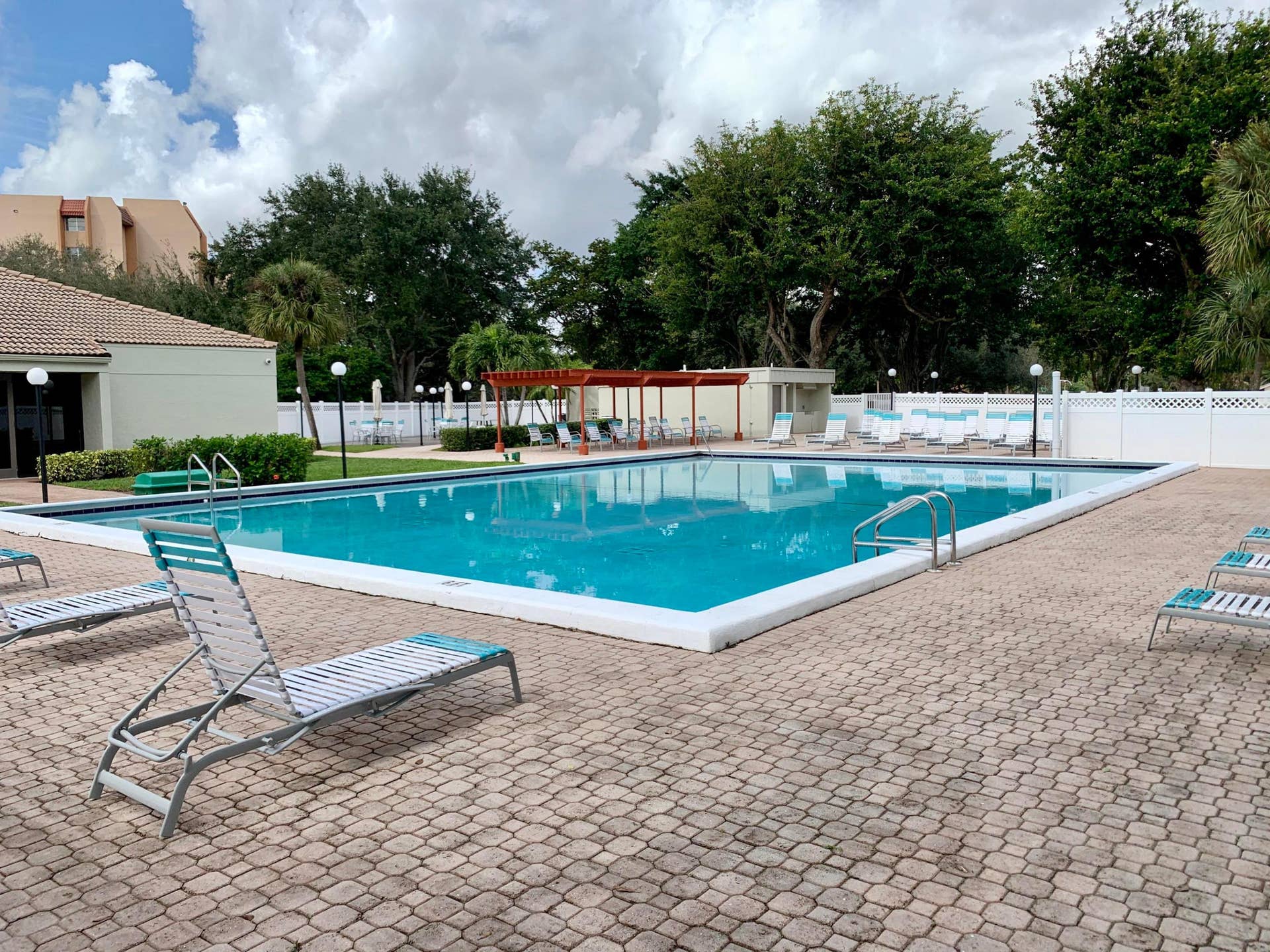 3100 W Rolling Hills Circle, #309, Davie, Davie, FL 33328 Spacious outdoor pool area featuring a rectangular pool with integrated steps, surrounding paver decking, and a white lattice fence