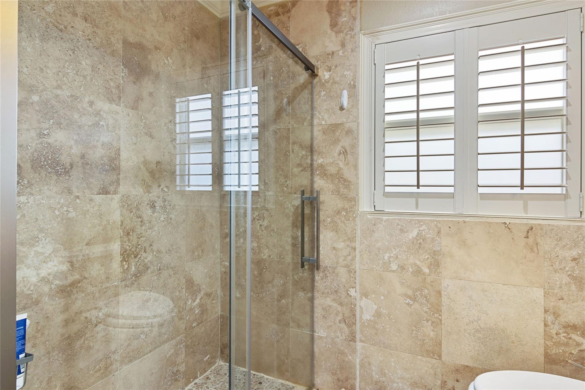Walk-in shower featuring glass enclosure, natural stone wall tiles, and pebbled floor