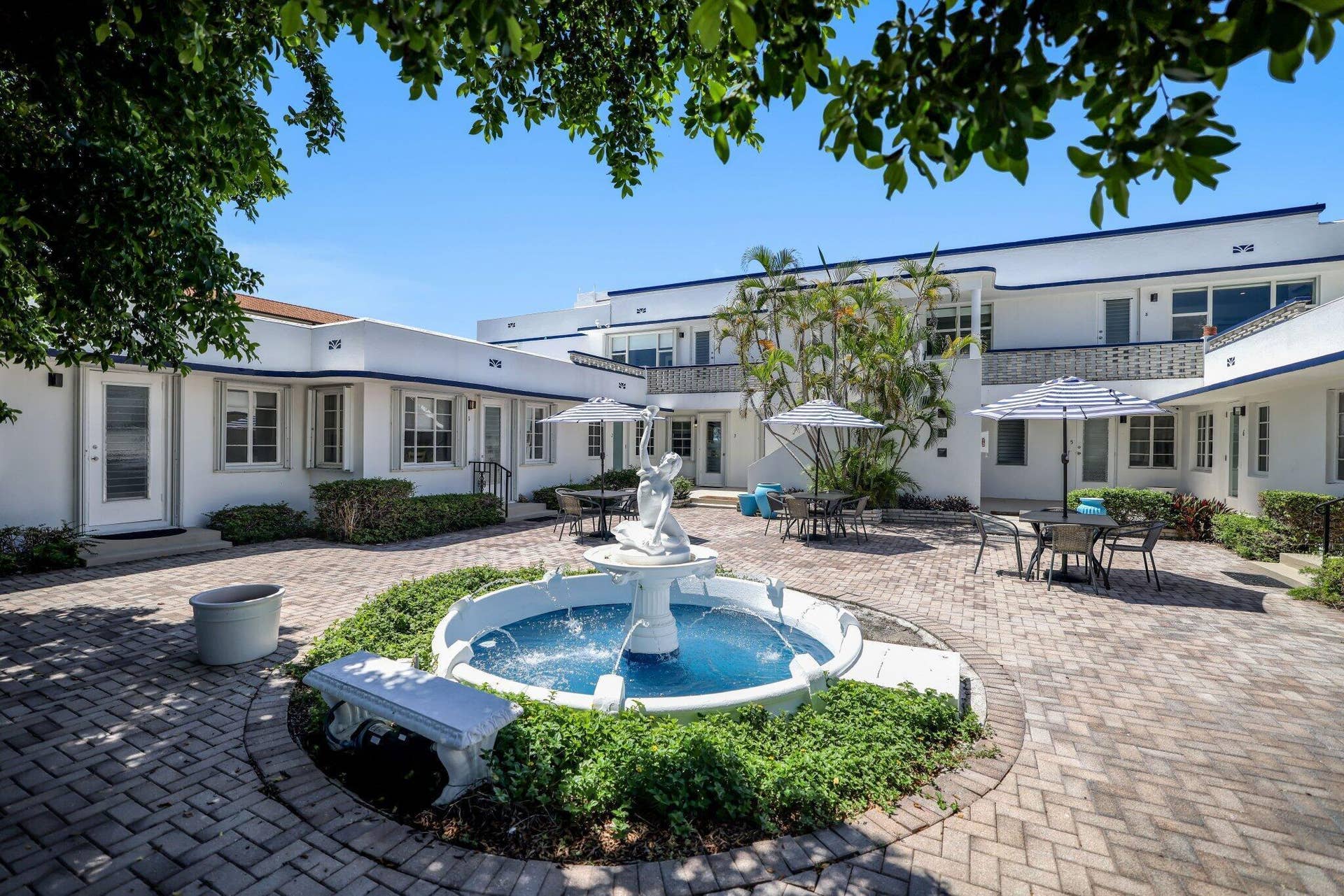 320 Inlet Way, #4, Palm Beach Shores, Palm Beach Shores, FL 33404 Courtyard featuring a multi-tiered fountain, herringbone brick paving, mature landscaping, and white stucco architectural elements with blue trim