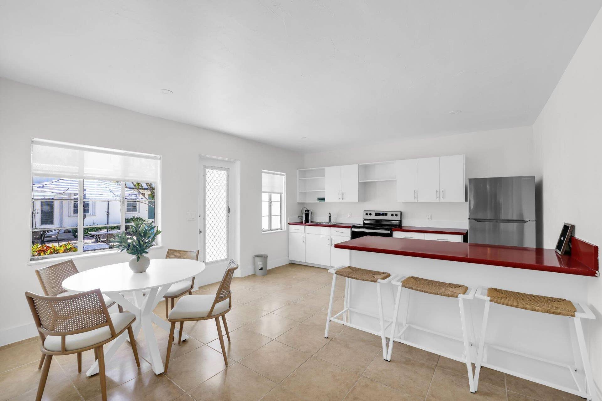 320 Inlet Way, #4, Palm Beach Shores, Palm Beach Shores, FL 33404 Open-concept kitchen and dining area featuring white cabinetry, contrasting red countertops, stainless steel appliances, and a breakfast bar