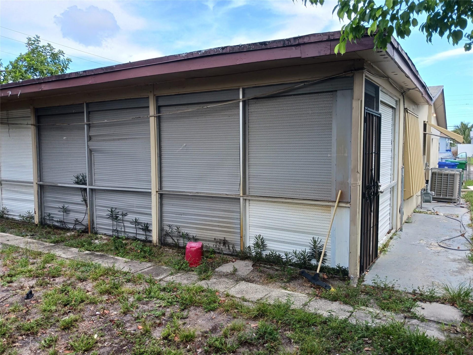 7757 SE EMBASSY Boulevard, Miramar, FL 33023 Exterior featuring multiple roll-down hurricane shutters, a covered walkway, and a side entrance with a security door