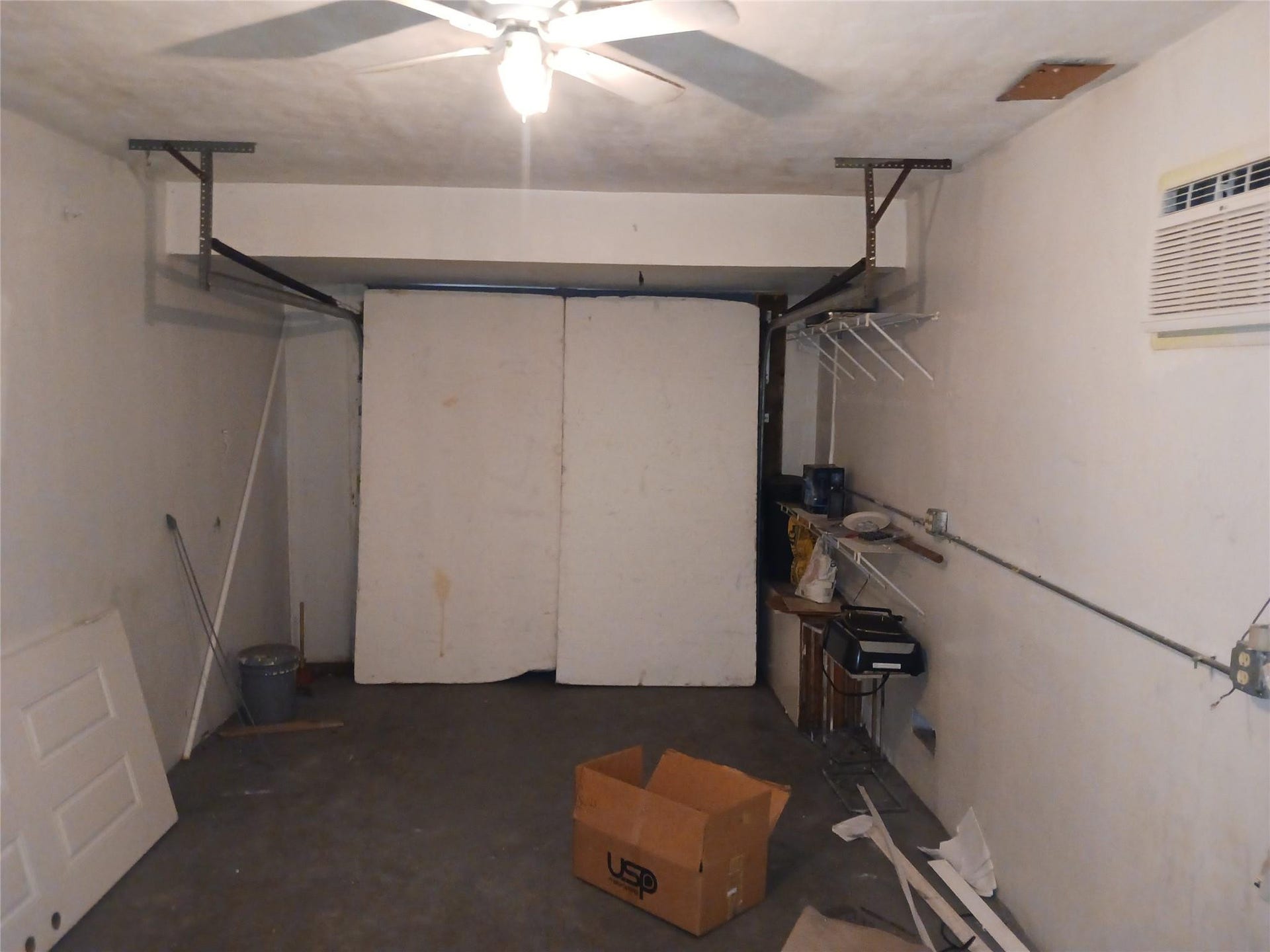 7757 SE EMBASSY Boulevard, Miramar, FL 33023 Garage interior featuring a ceiling fan with integrated lighting, a wall-mounted air conditioning unit, and exposed ceiling joists