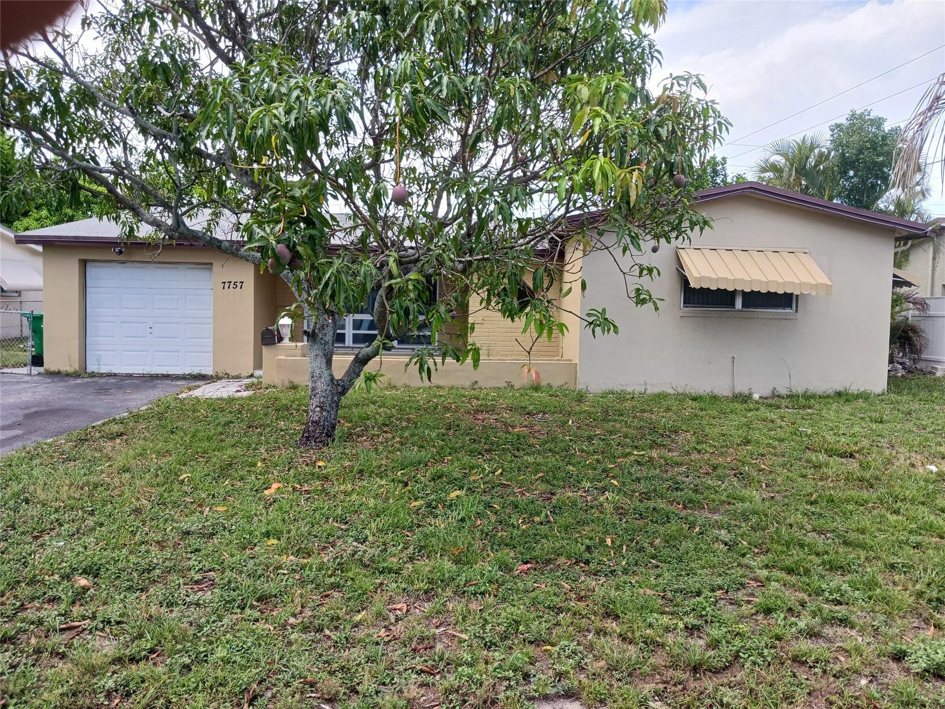 7757 SE EMBASSY Boulevard, Miramar, FL 33023 Exterior featuring a neutral stucco finish, white garage door, and a prominent front-facing tree