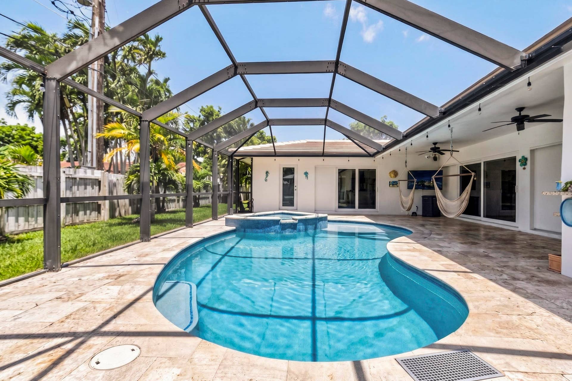 Screened-in outdoor area featuring a freeform pool with an integrated spa, extensive stone paver decking, and a covered patio with ceiling fans and recessed lighting