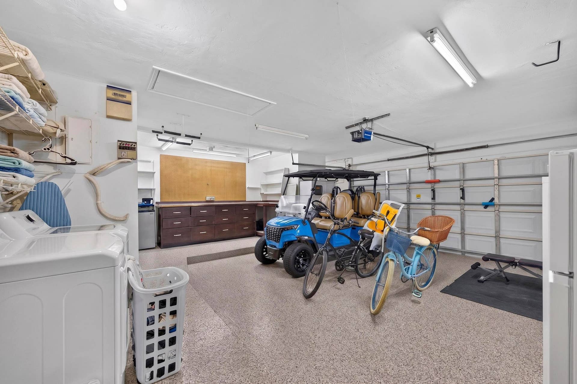 Spacious garage featuring a durable speckled epoxy floor, large alcove with built-in workbench, storage, fluorescent overhead lighting, and white paneled garage doors