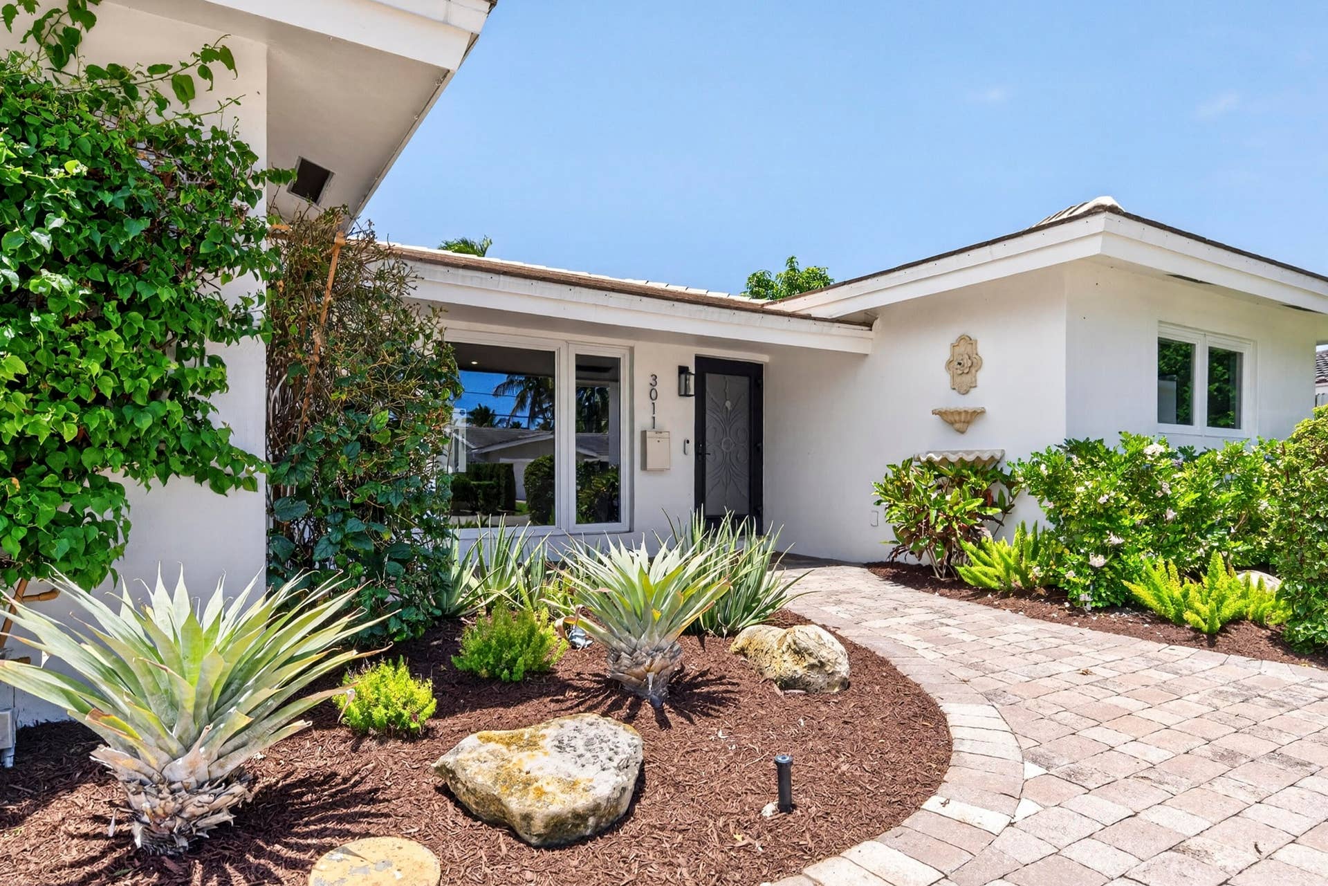 White stucco exterior with a dark entry door, framed by a paver walkway
