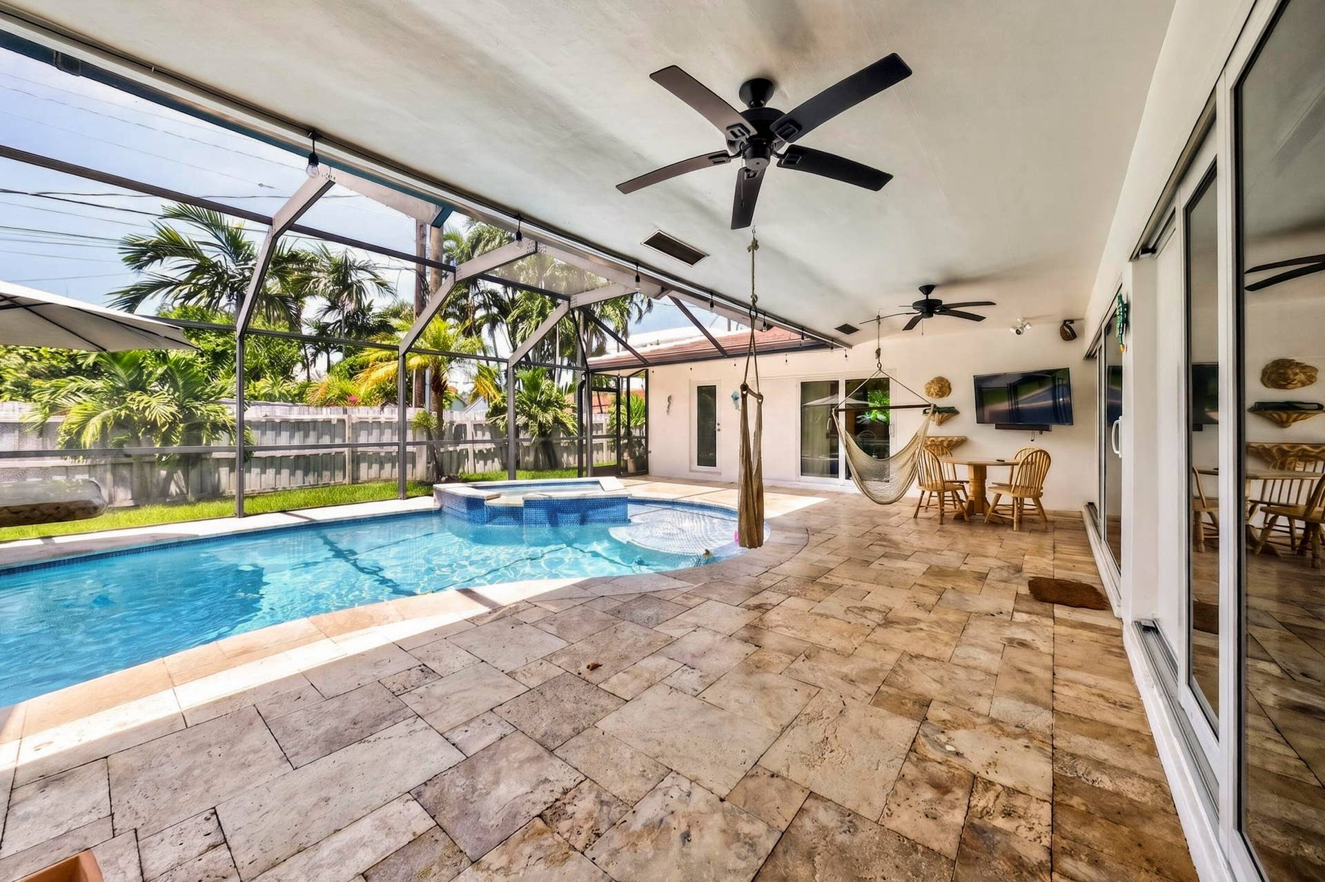 Screened patio featuring a swimming pool with attached spa, extensive stone-finish flooring, and multiple ceiling fans