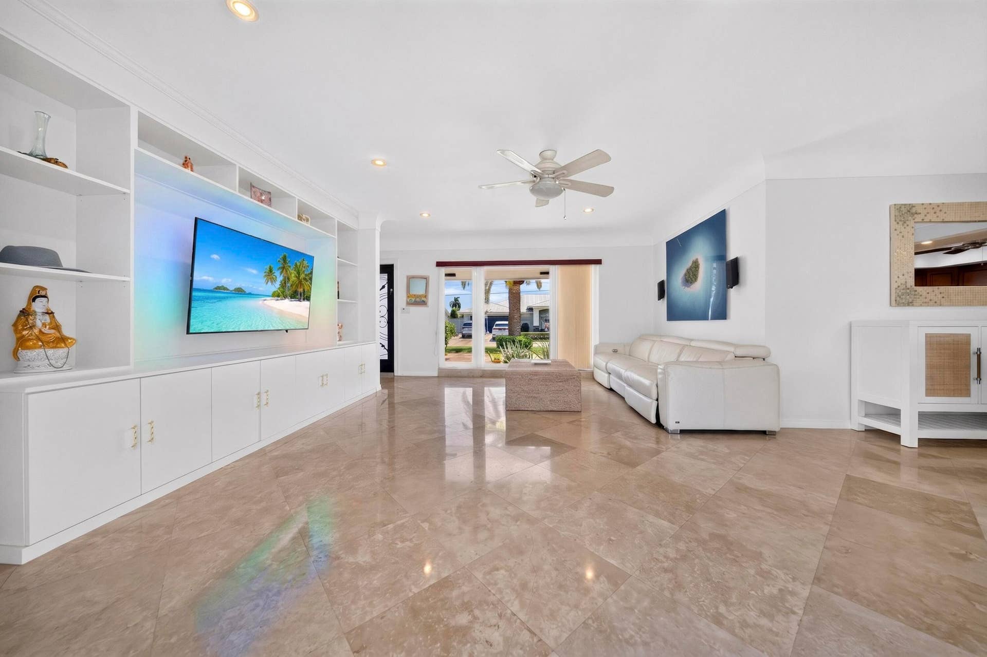 Spacious living area featuring polished Travertine marble flooring, a built-in entertainment center with open shelving and lower cabinetry, a ceiling fan, recessed lighting, and a wide entryway with double glass doors