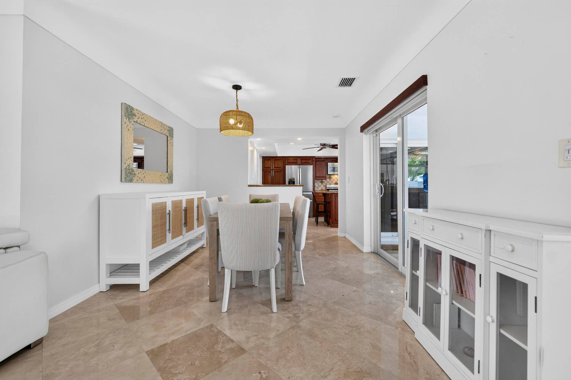 Dining area featuring tile flooring, a woven pendant light fixture, white walls, and sliding glass doors providing access to the exterior