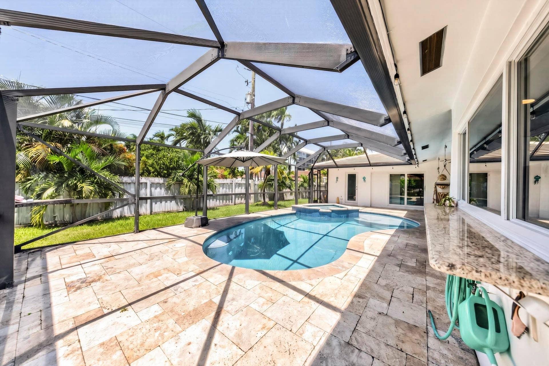 Screened outdoor living area featuring a freeform swimming pool with integrated spa, extensive stone paver decking, and a built-in outdoor bar with a stone countertop