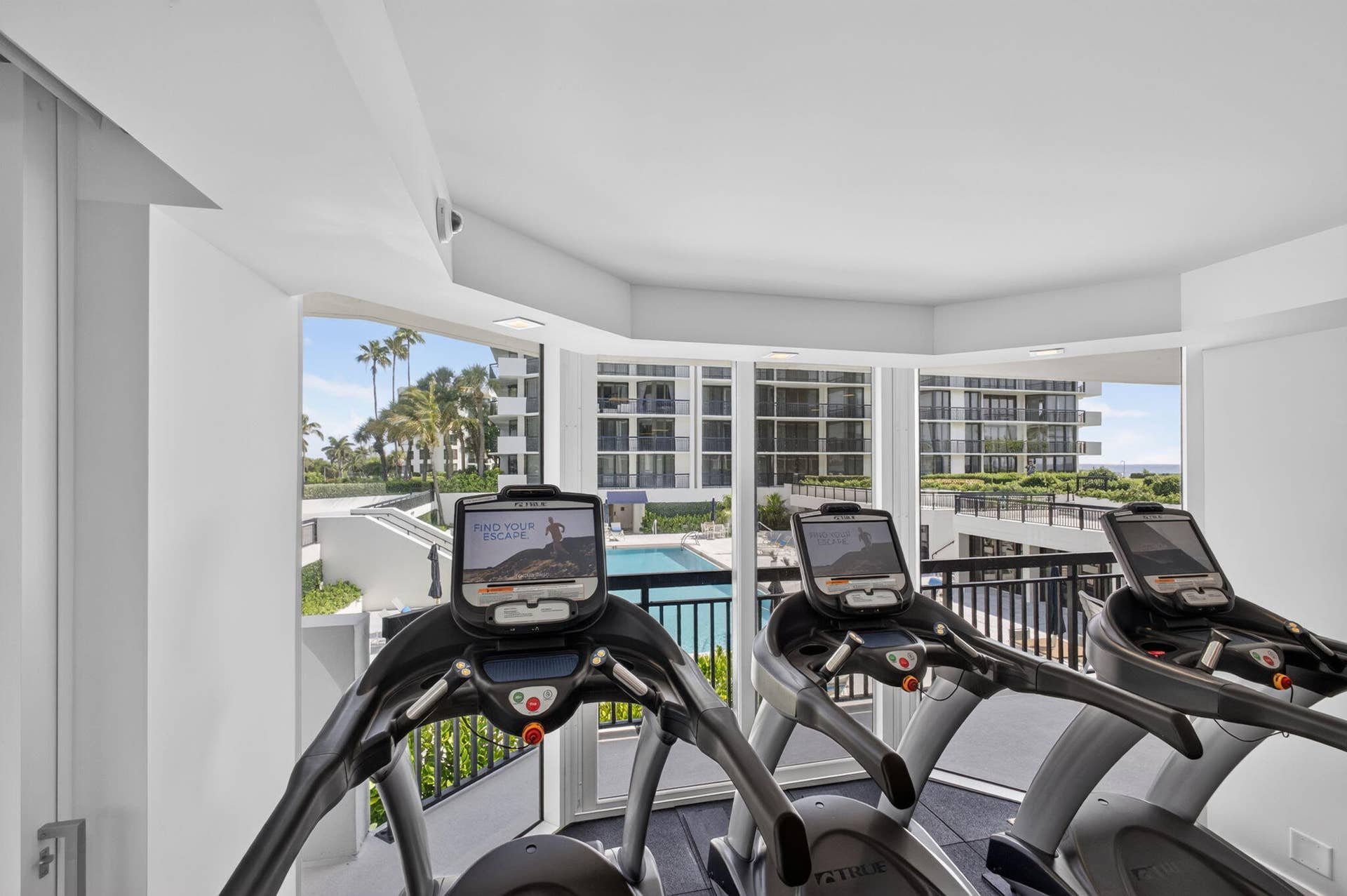3140 S Ocean Boulevard, #101 S, Palm Beach, FL 33480 Fitness area featuring floor-to-ceiling windows, panoramic outdoor scenery, a swimming pool, and tropical foliage