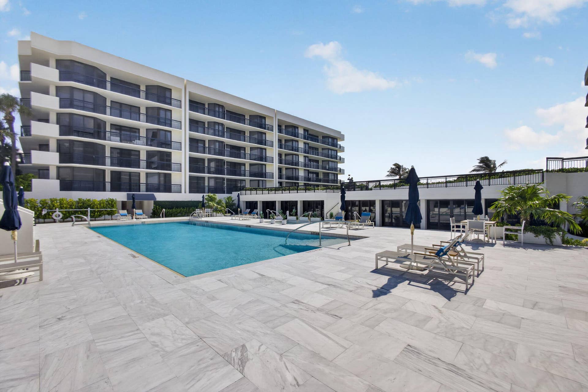 3140 S Ocean Boulevard, #101 S, Palm Beach, FL 33480 Expansive pool deck featuring a rectangular swimming pool, light-toned stone tile flooring, and a multi-story building with private balconies