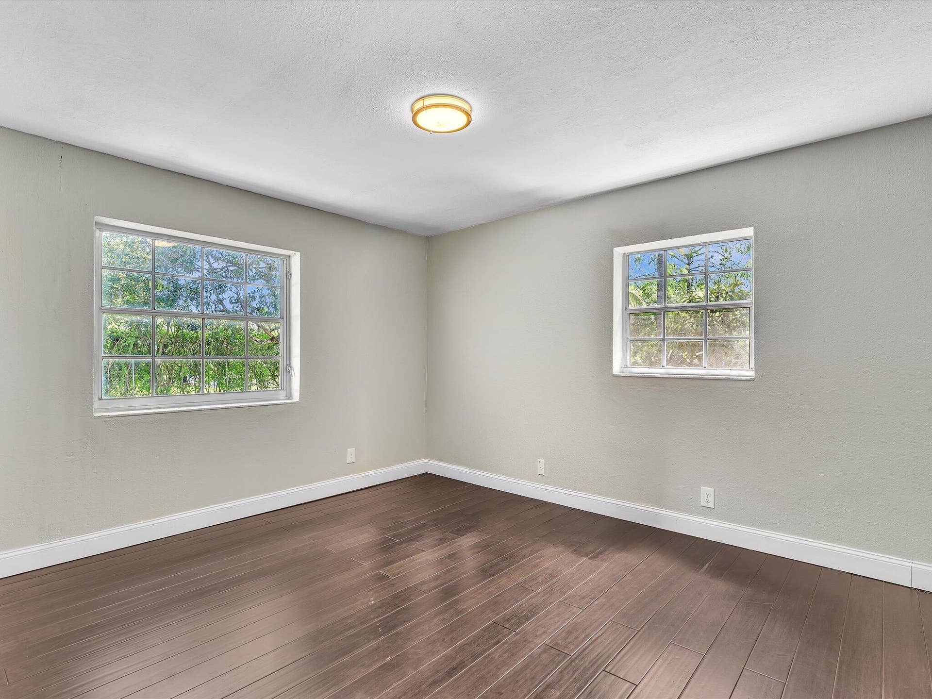 Spacious room featuring rich wood-finish flooring, light gray walls, white baseboards, and a contemporary ceiling light fixture