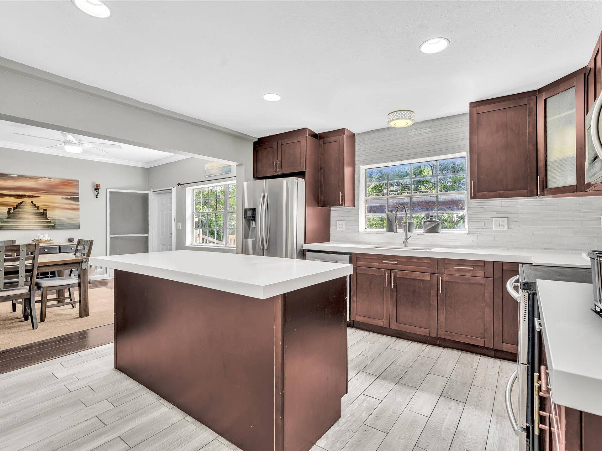 Contemporary kitchen featuring a center island with a white countertop, recessed lighting, wood-finish cabinetry, stainless steel appliances, and tile flooring