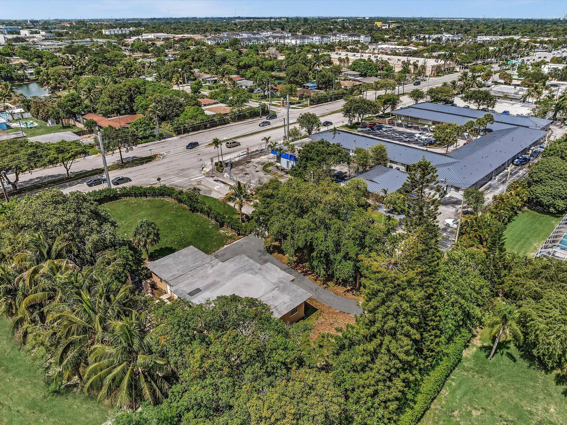 Aerial perspective showcasing a property surrounded by mature trees, a manicured lawn area, and a paved driveway