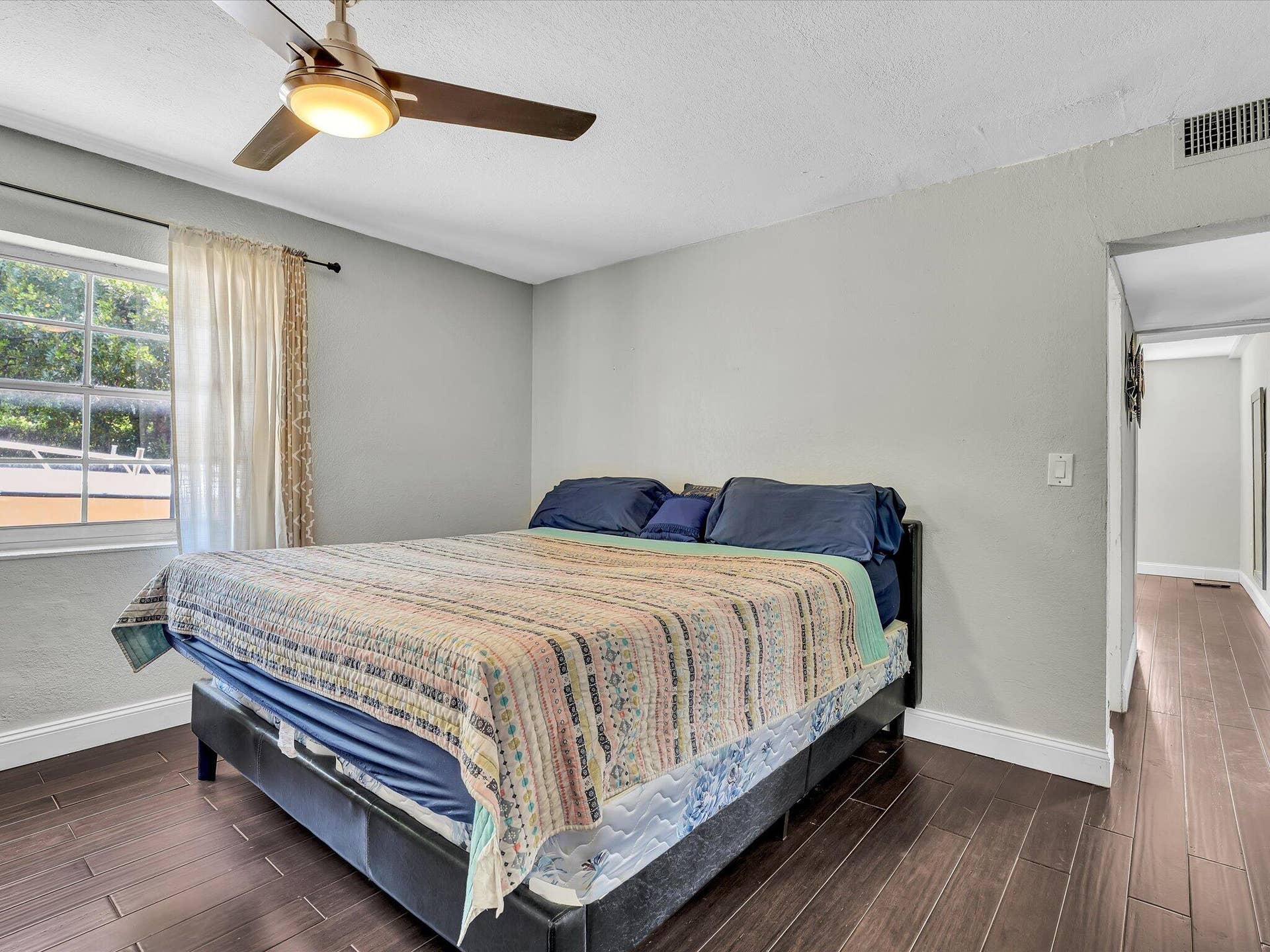 Room featuring wood-finish flooring, a ceiling fan with integrated lighting, a window with a curtain rod, and a white baseboard trim
