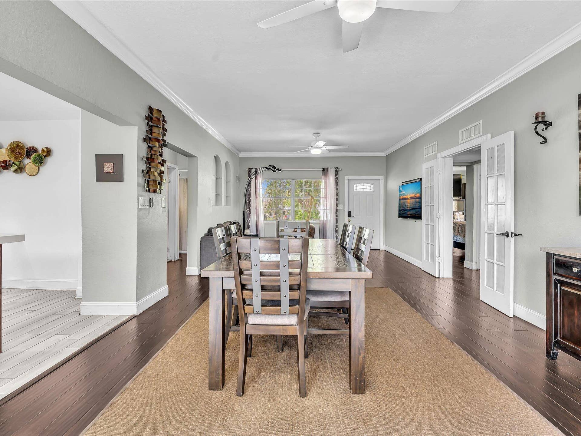 Open-concept dining area featuring dark wood-finish flooring, white crown molding, and a ceiling fan with integrated lighting