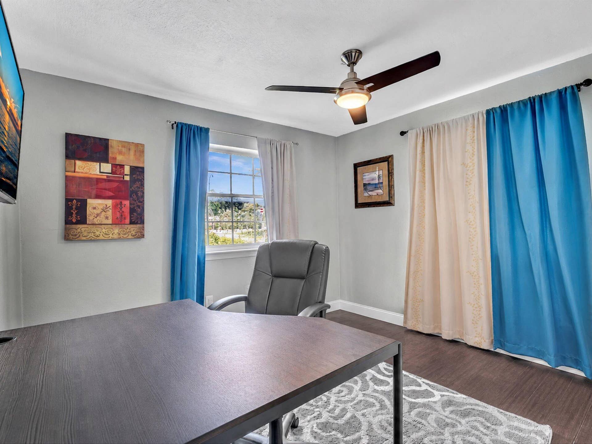 Bright room featuring a window with exterior views, dark wood-finish flooring, and a ceiling fan with integrated lighting