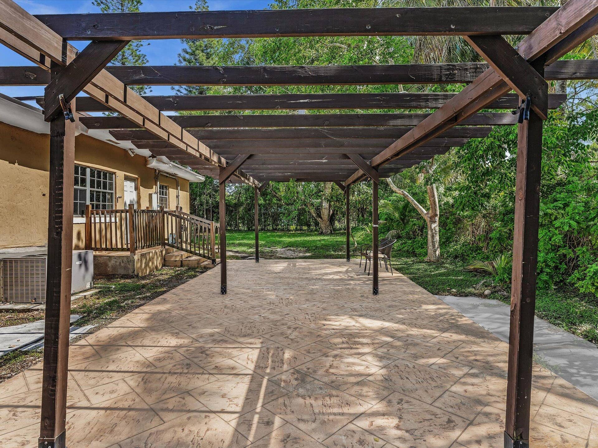 Expansive covered patio featuring a dark wood pergola, stamped concrete flooring, and direct access to an exterior wooden staircase