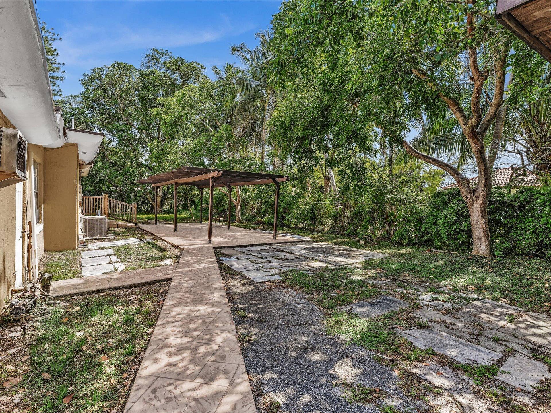 Expansive outdoor area featuring a pergola-covered patio, concrete pathways, and lush mature trees