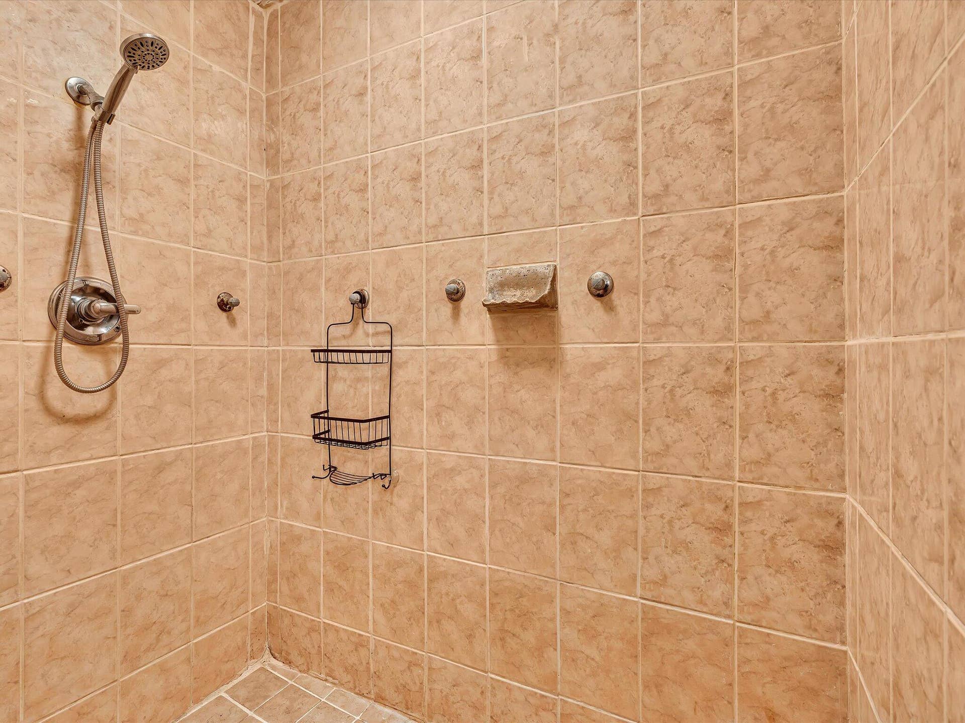 Shower enclosure featuring full-height tiled walls and floor, a handheld shower fixture, and a built-in soap dish