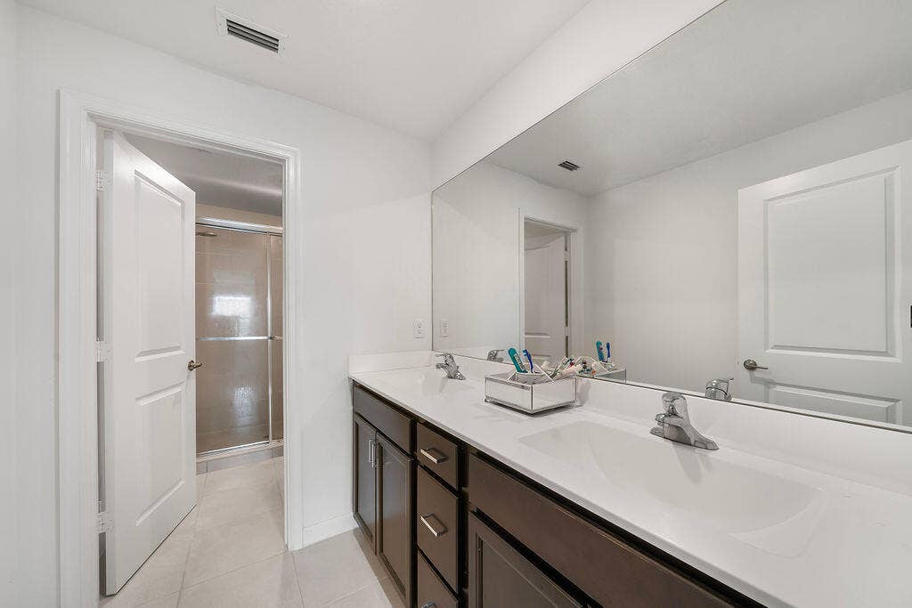 Bathroom featuring a dual vanity with dark wood-finish cabinetry, white countertops, and a full-width mirror
