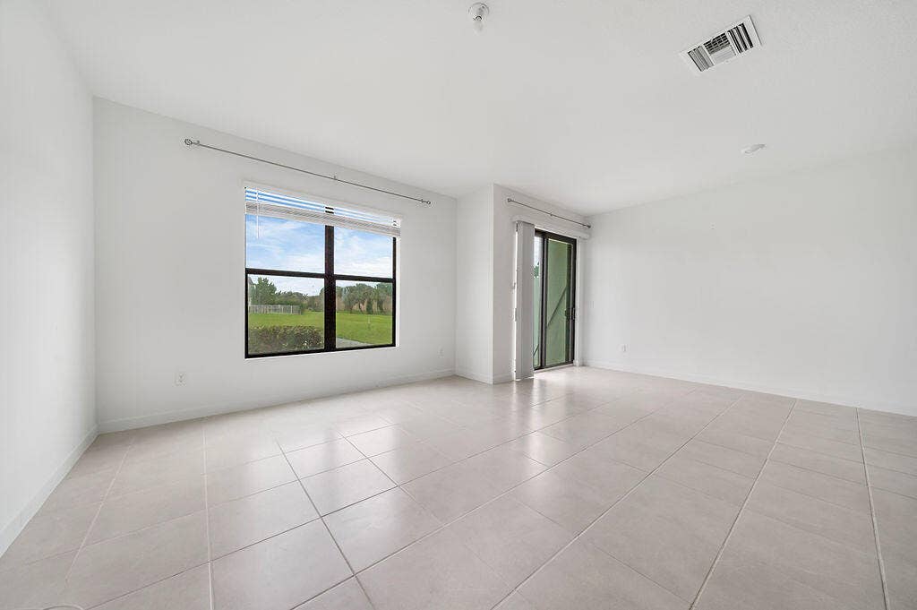 Spacious room featuring light-toned tile flooring, a large window with horizontal blinds, and a sliding glass door