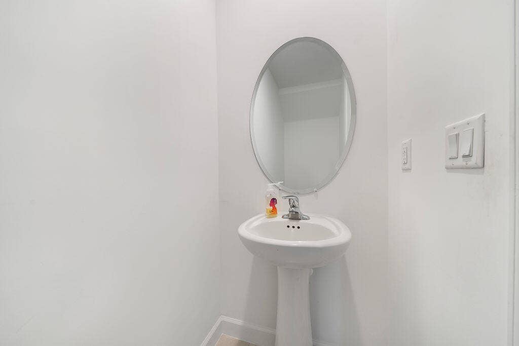 Pedestal sink with chrome faucet, complemented by an oval wall-mounted mirror