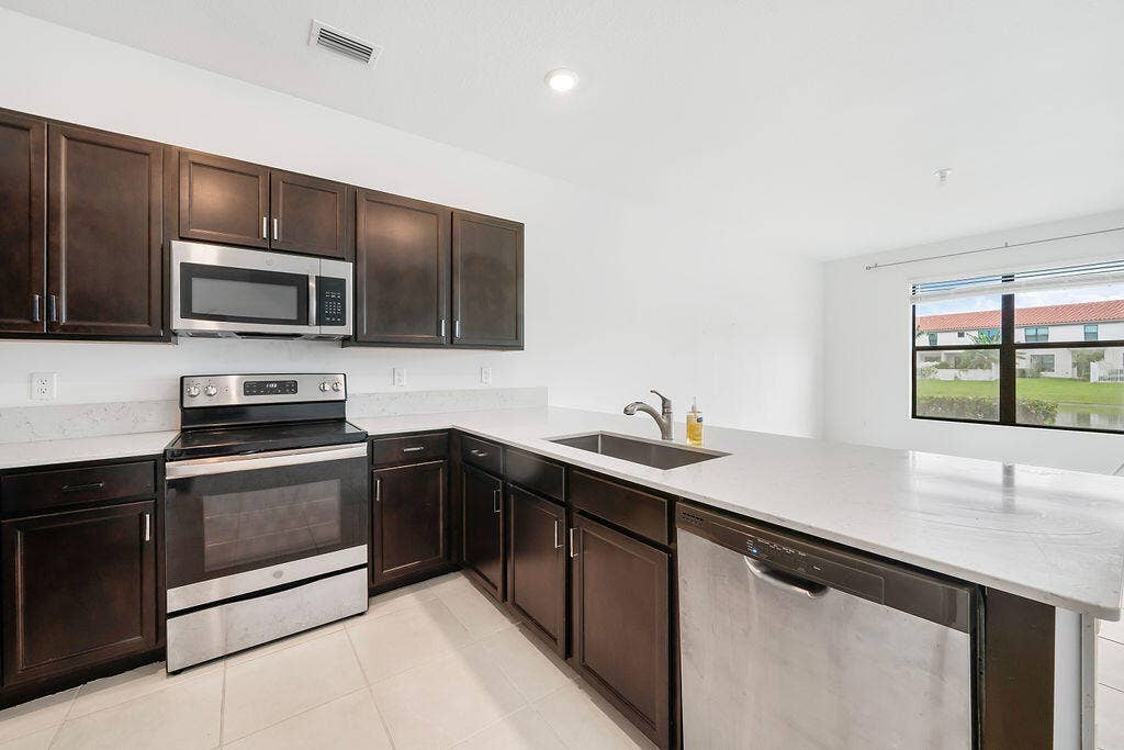 Kitchen featuring dark wood cabinetry, light-toned countertops, snack bar, stainless steel appliances, pantry, and recessed lighting