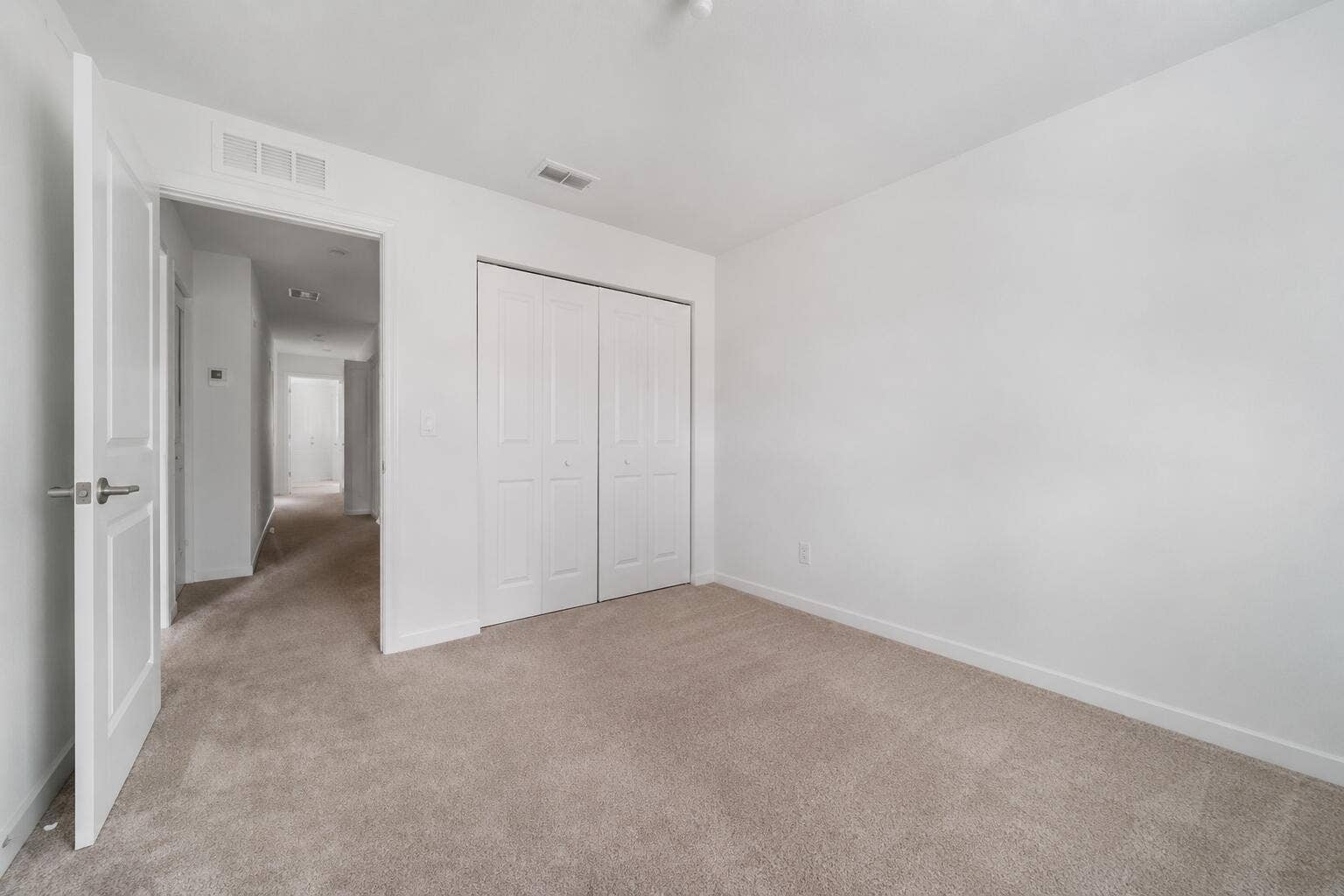 Carpeted room featuring a double bifold closet, white walls, and white trim