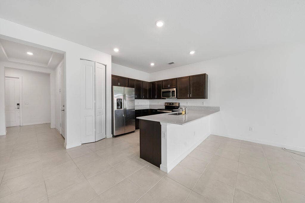 Kitchen featuring dark wood cabinetry, light-toned countertops, snack bar, stainless steel appliances, pantry, and recessed lighting