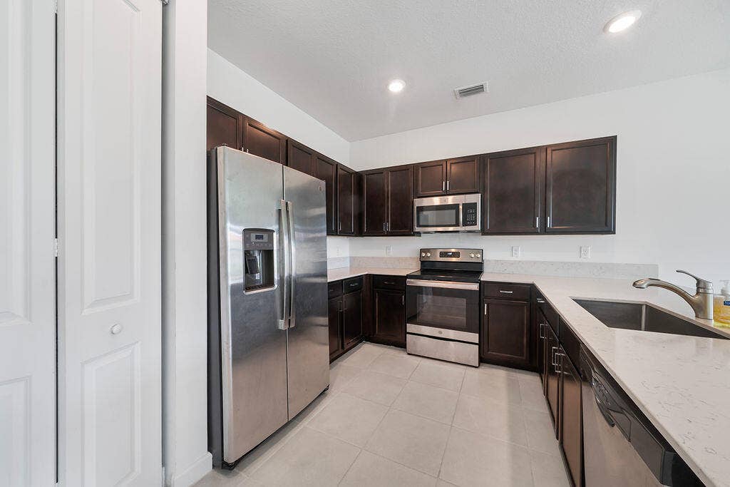 Kitchen featuring dark wood cabinetry, light-toned countertops, snack bar, stainless steel appliances, pantry, and recessed lighting