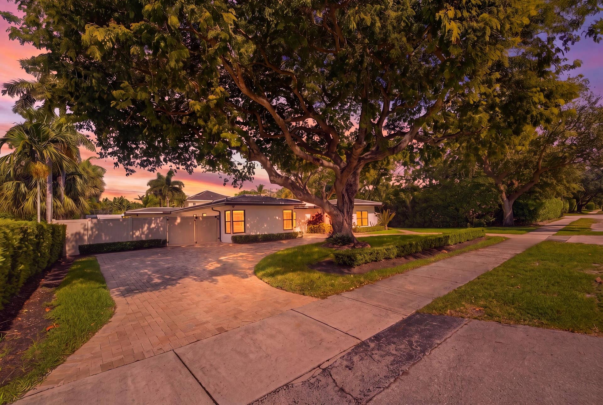 Expansive paver driveway with surrounding lush landscaping and mature trees