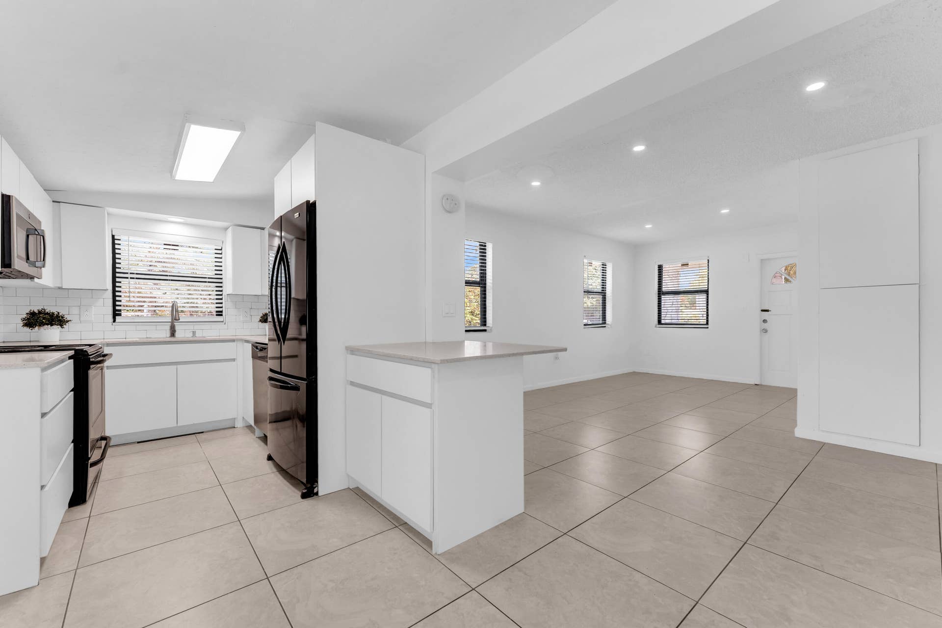 Open-concept living area featuring a modern kitchen with white cabinetry, stainless steel appliances, and a subway tile backsplash