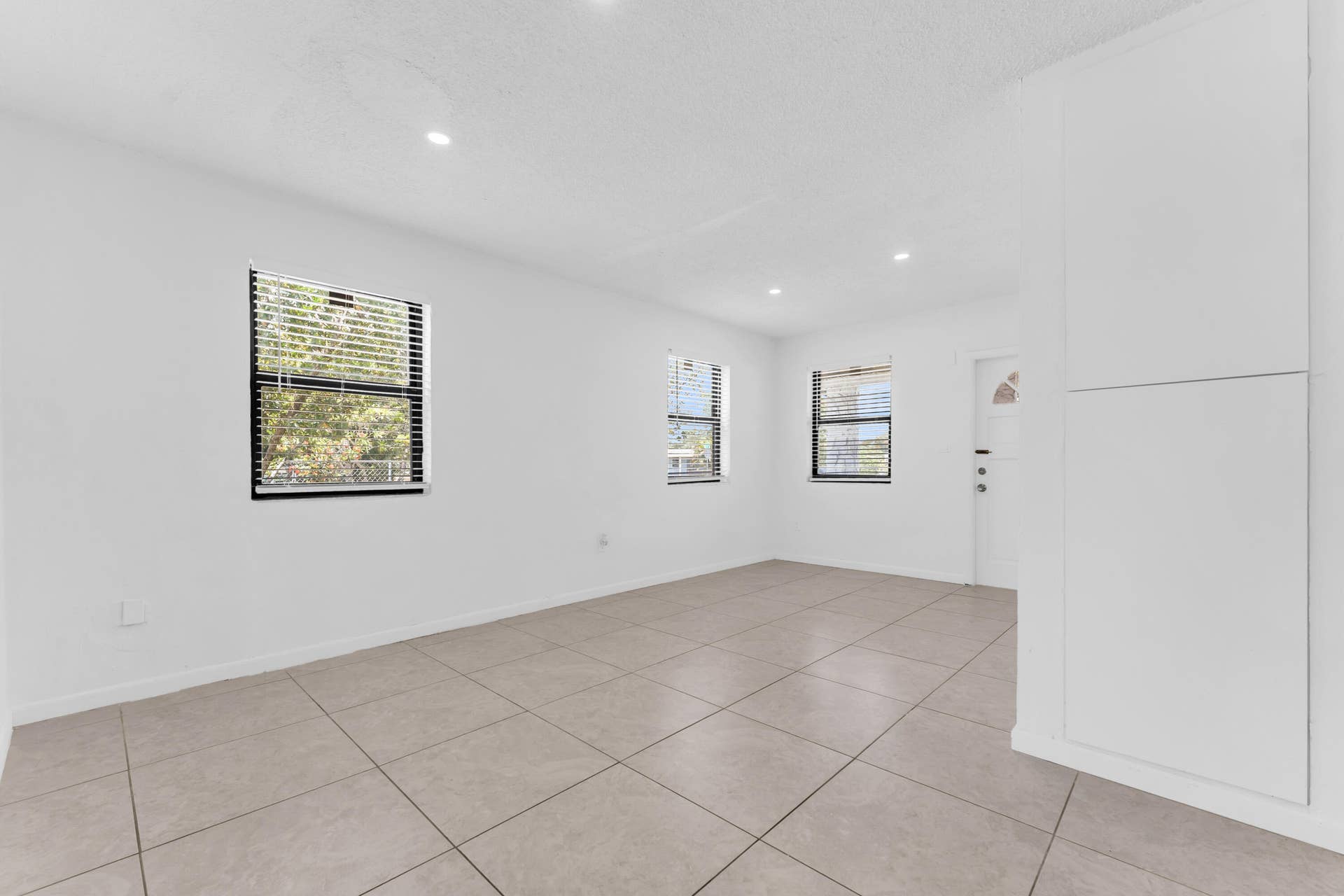Spacious interior featuring neutral tile flooring, recessed lighting, multiple windows with blinds, and built-in cabinetry