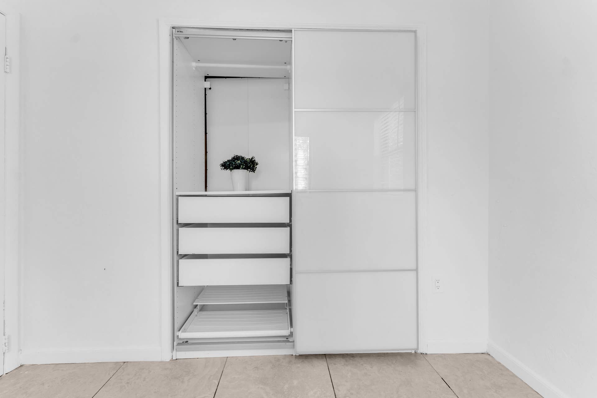 Built-in closet system featuring white sliding doors with frosted glass panels, an internal hanging rod, multiple drawers, and pull-out shelving