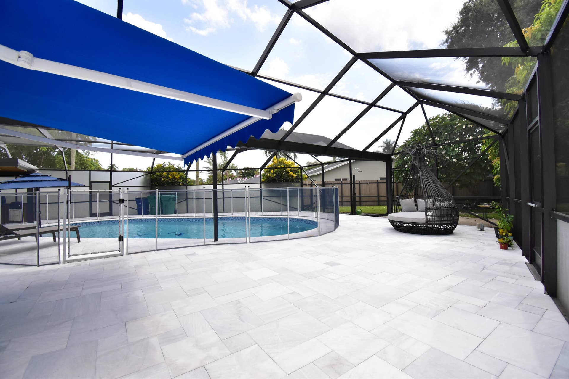 5061 SW 87TH Terrace, Cooper City, FL 33328 Spacious screened patio featuring an enclosed swimming pool, a blue retractable awning, a safety fence around the pool, and a light-toned paver deck