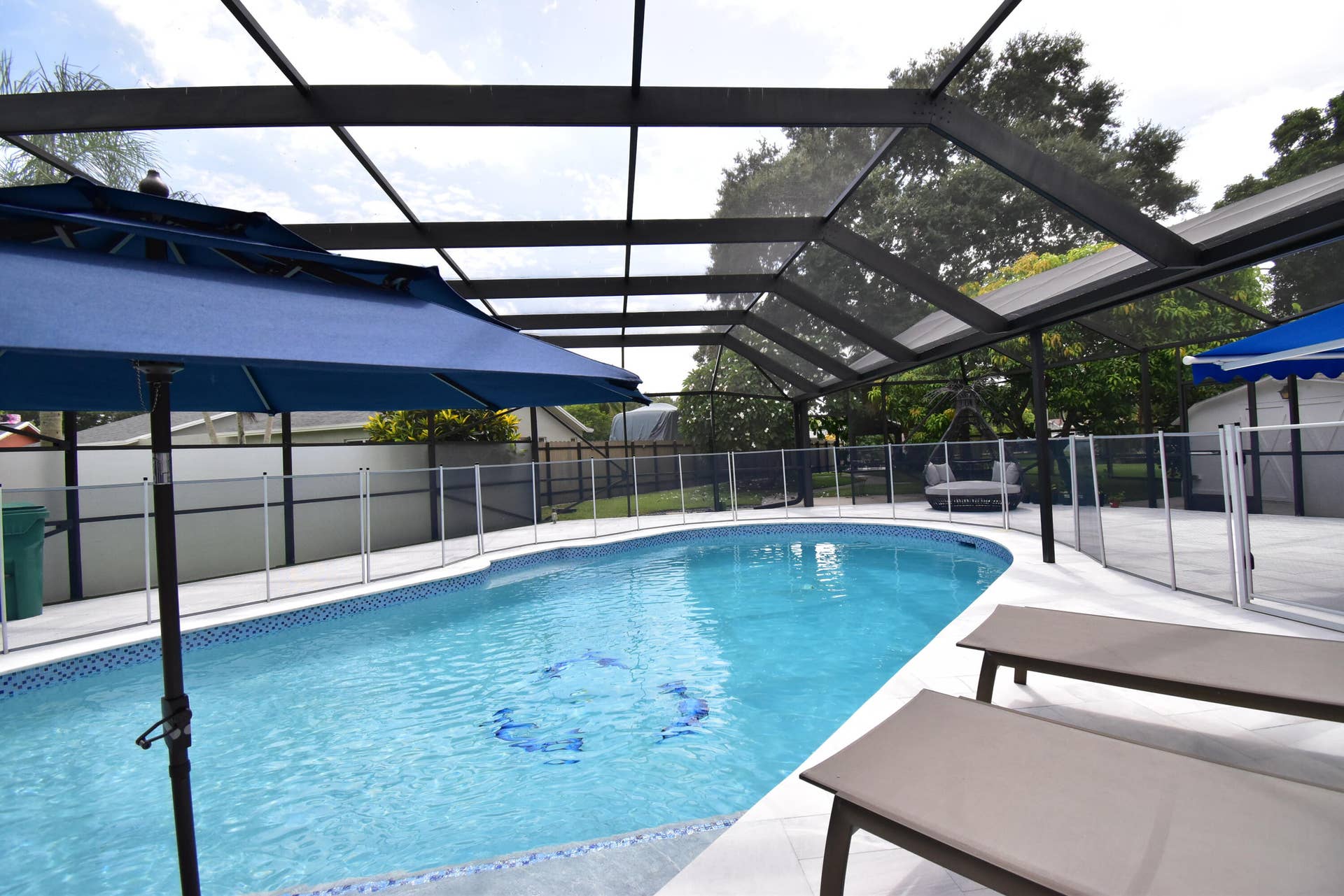 5061 SW 87TH Terrace, Cooper City, FL 33328 Screened enclosure featuring a freeform swimming pool with blue tile accents, a surrounding pool deck, and a perimeter safety fence