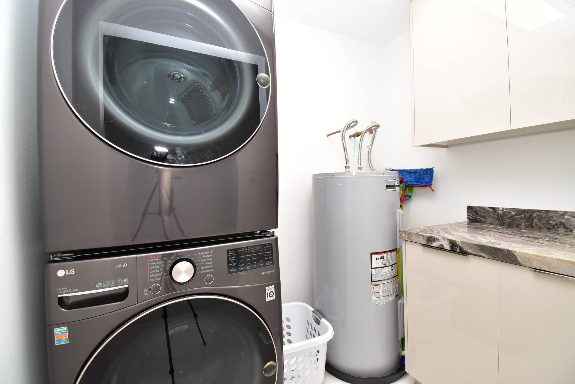 5061 SW 87TH Terrace, Cooper City, FL 33328 Laundry area featuring a stacked front-load washer and dryer, a water heater, a stone-finish countertop, and upper and lower cabinetry with integrated pulls