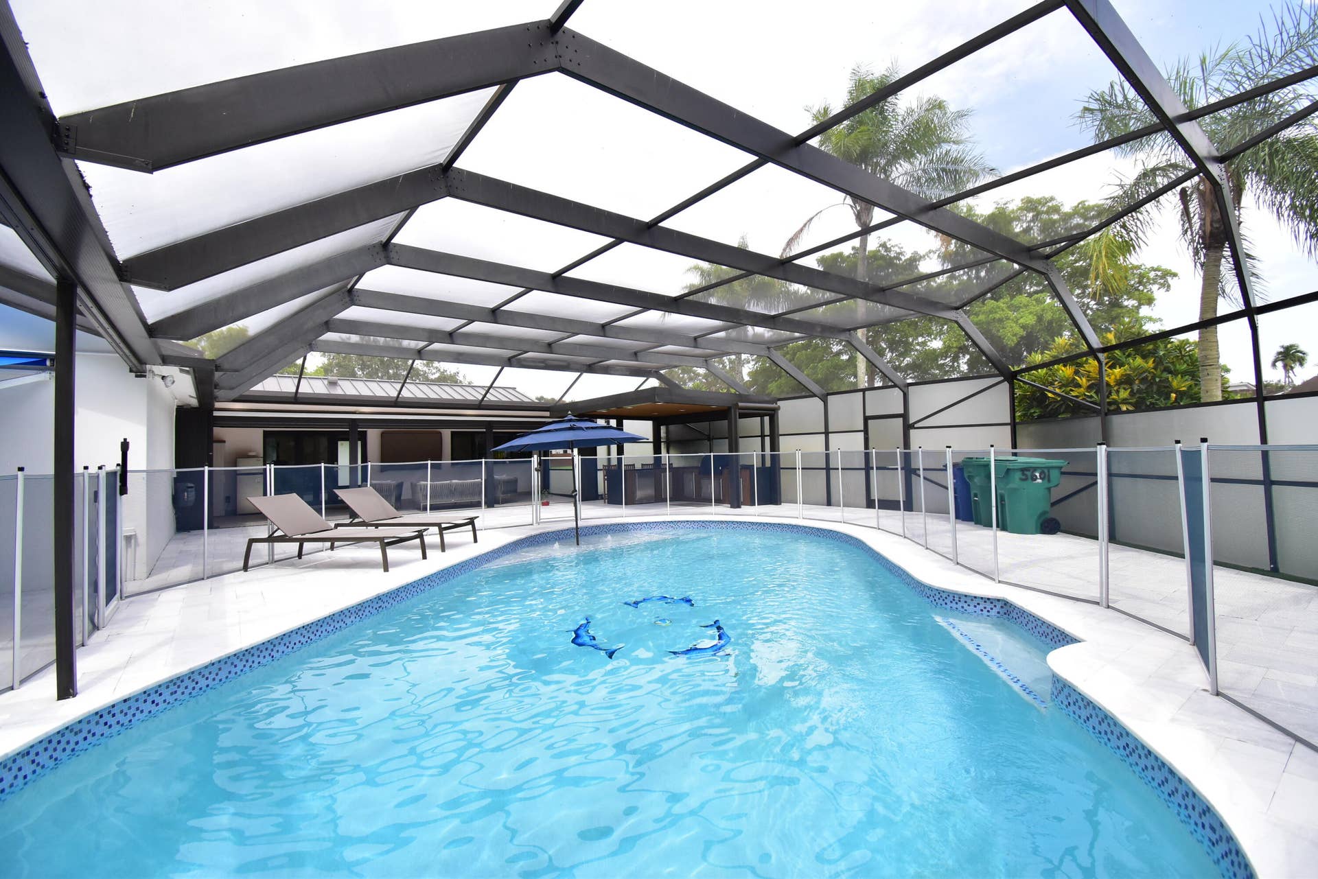 5061 SW 87TH Terrace, Cooper City, FL 33328 Screened pool enclosure featuring an irregular shaped pool with blue mosaic tile trim, light-colored paver decking, and a removable perimeter fence