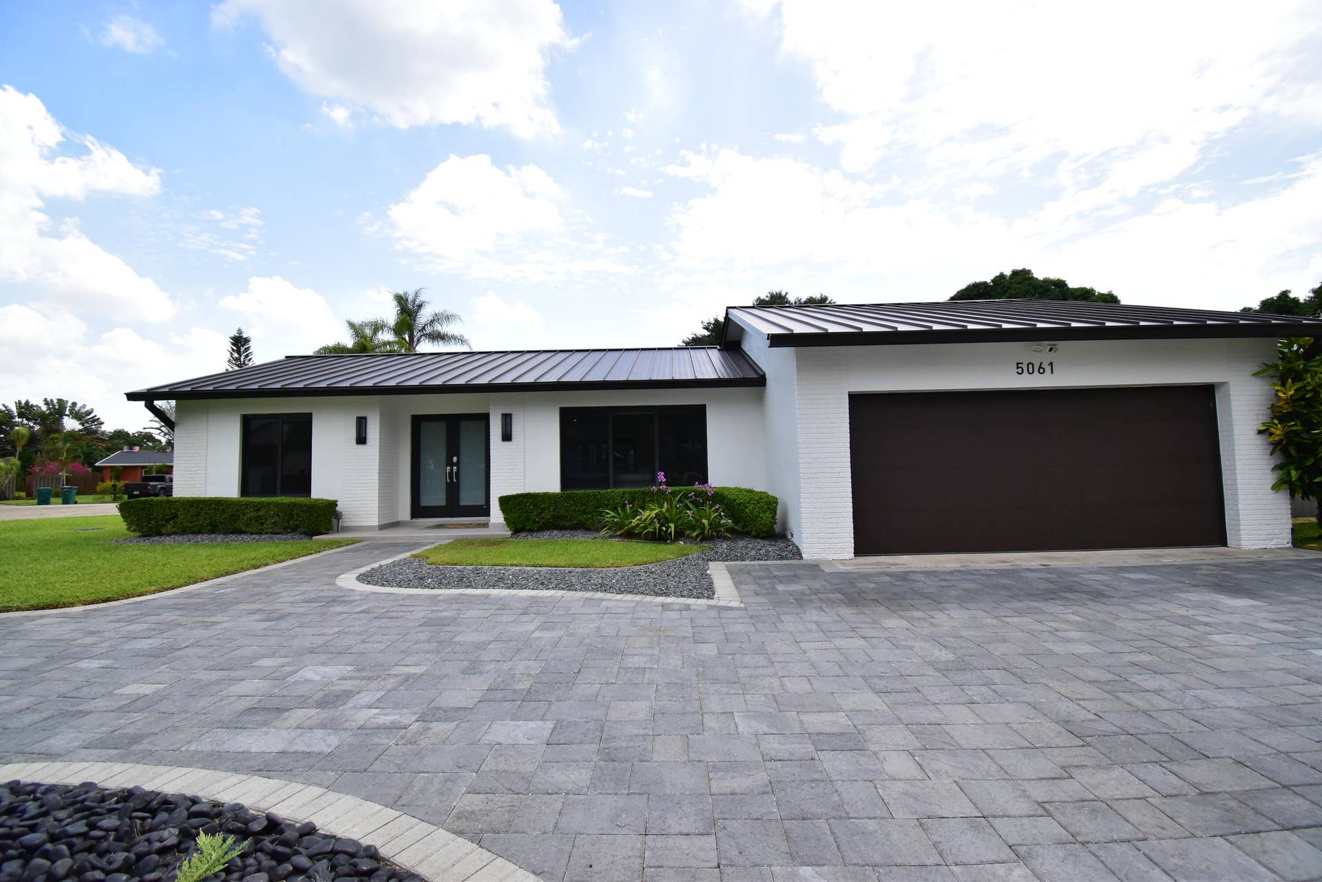 5061 SW 87TH Terrace, Cooper City, FL 33328 Contemporary white brick exterior featuring a dark metal roof, a paved driveway, manicured landscaping, and a two-car garage