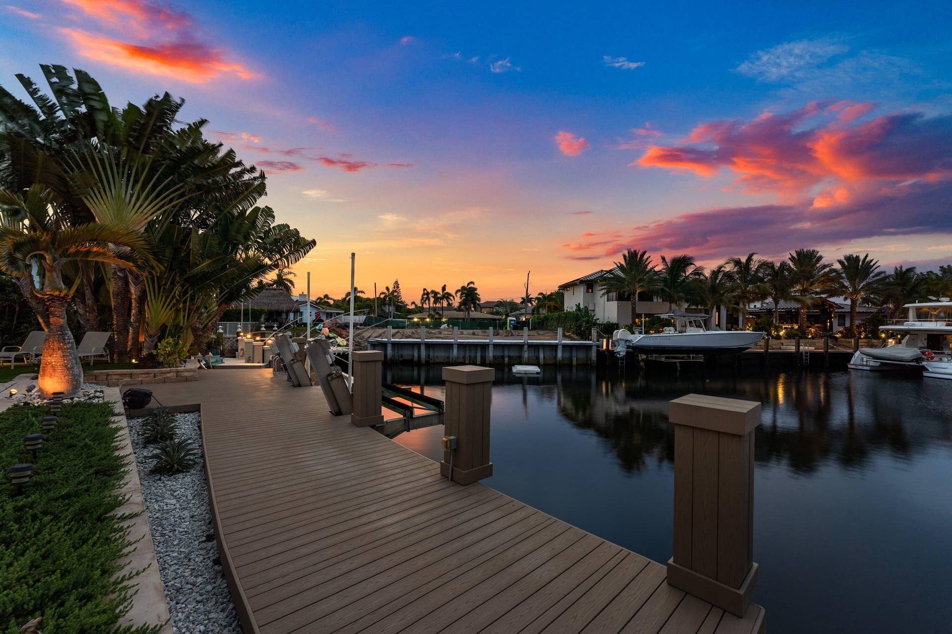 2761 NE 48TH Court, Lighthouse Point, FL 33064 Waterfront property featuring an expansive composite deck, mature palm trees, integrated landscape lighting, and a private boat slip