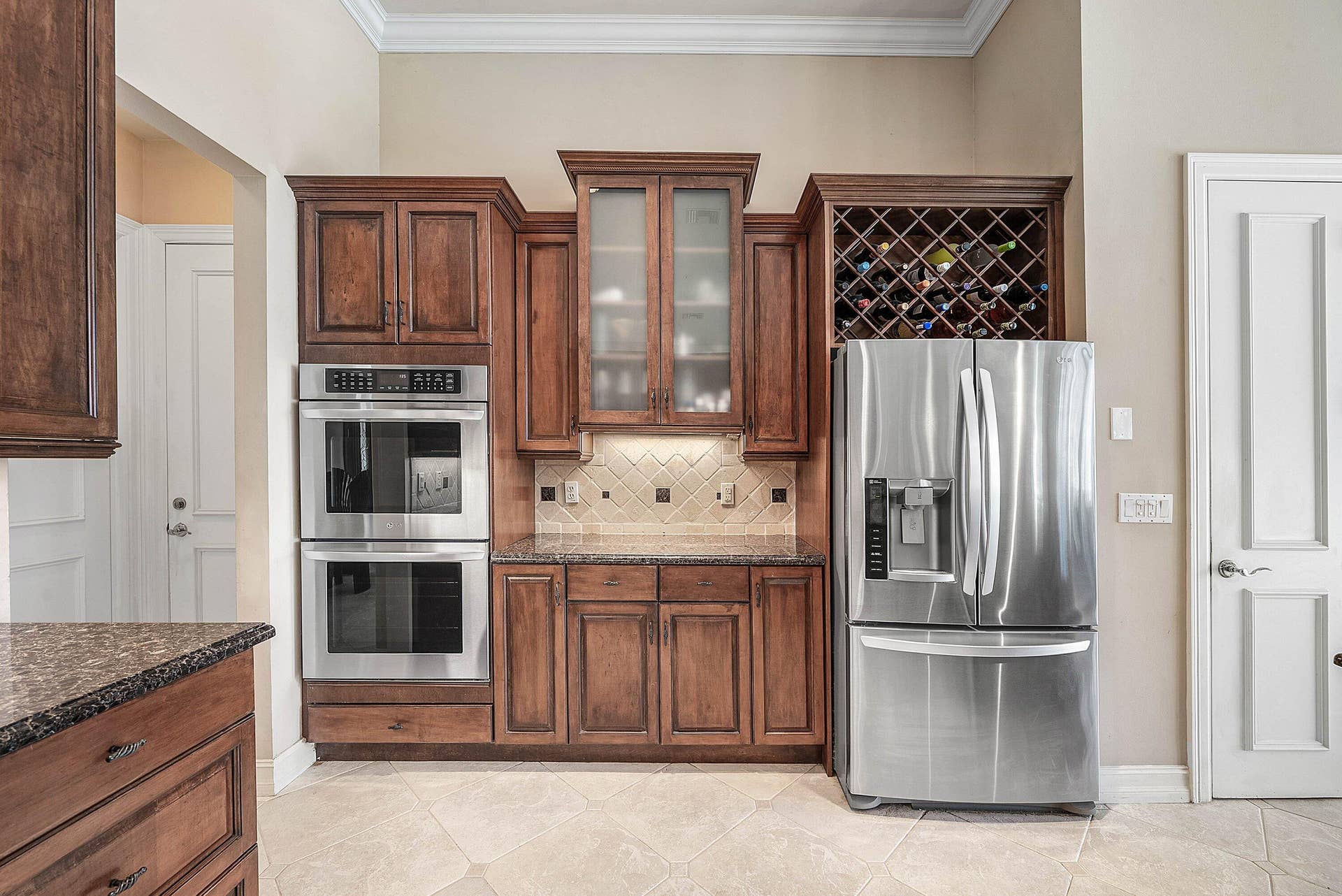 2761 NE 48TH Court, Lighthouse Point, FL 33064 Kitchen appliance wall featuring dark wood-finish cabinetry, stainless steel double ovens, a built-in wine rack, a French door refrigerator, and a tiled backsplash