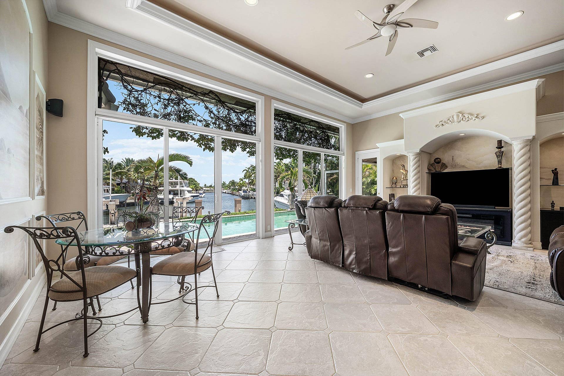 2761 NE 48TH Court, Lighthouse Point, FL 33064 Spacious living area featuring large windows overlooking a waterfront, tile flooring, and a decorative built-in entertainment center with architectural columns
