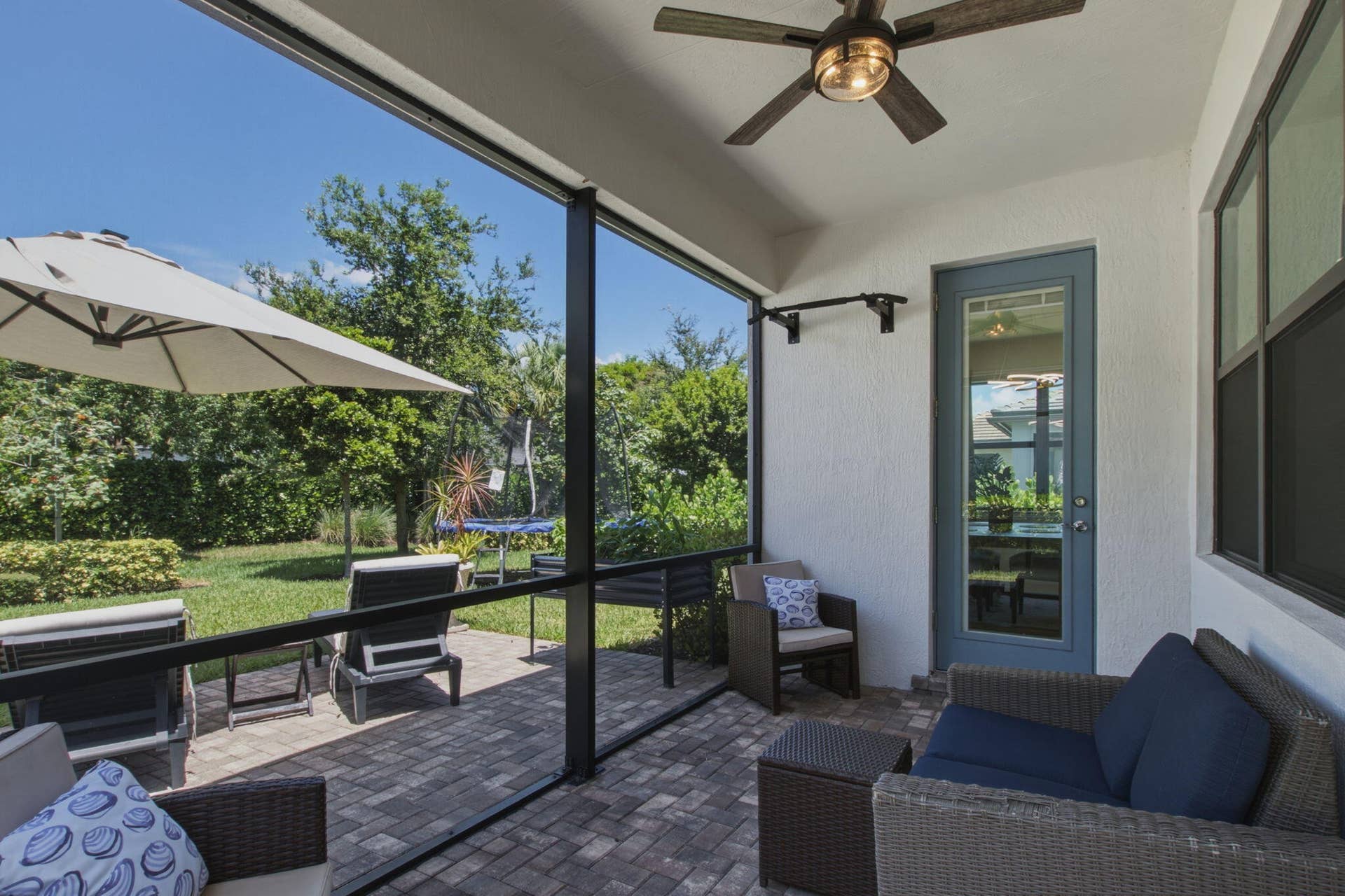 4601 Pinehurst Trail E, Oakland Park, FL 33309 Screened patio featuring paver flooring, a ceiling fan, a glass-paneled door, and a private backyard with mature landscaping