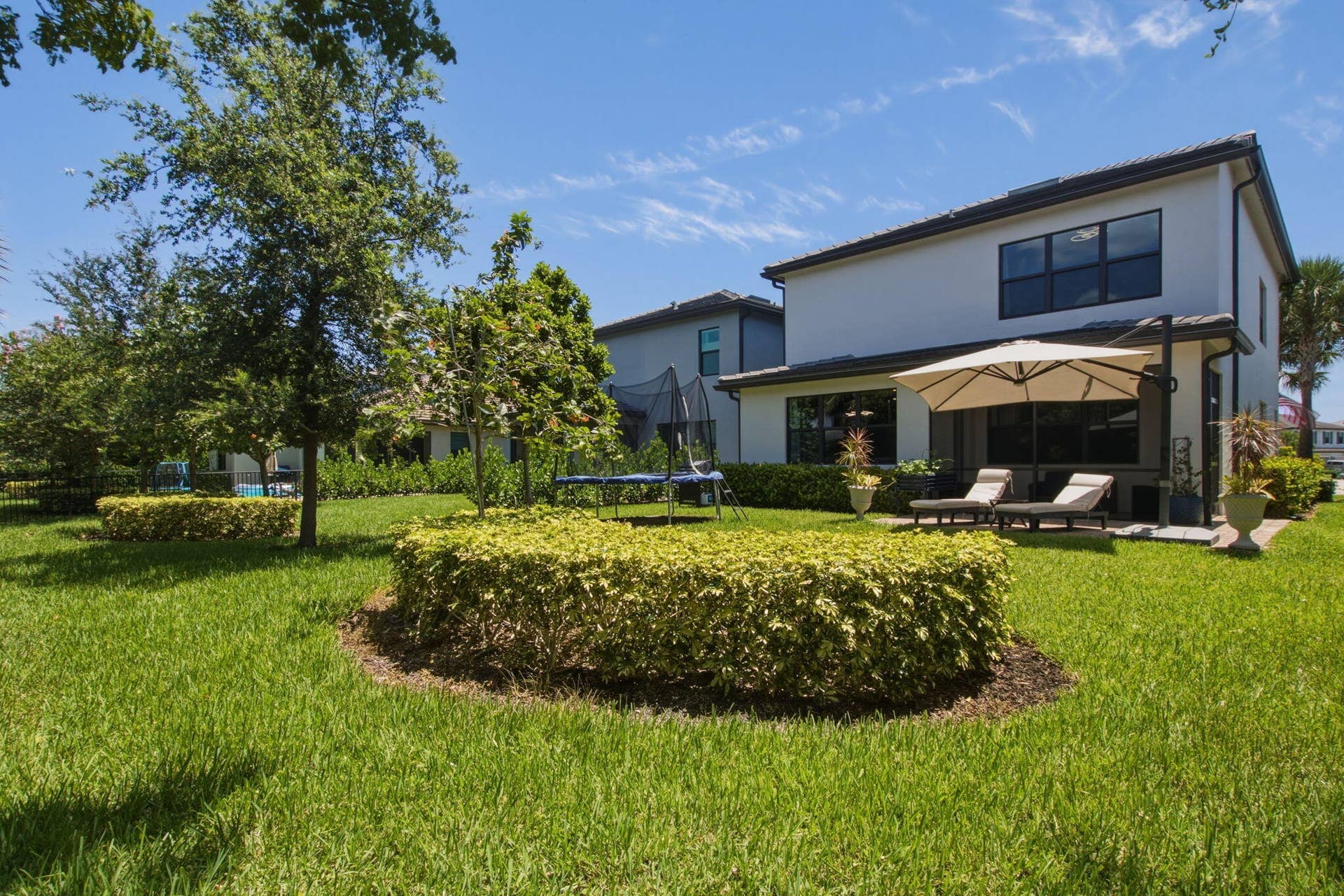4601 Pinehurst Trail E, Oakland Park, FL 33309 Rear exterior showcasing a white stucco facade with dark-framed windows, a covered patio, and a spacious green lawn