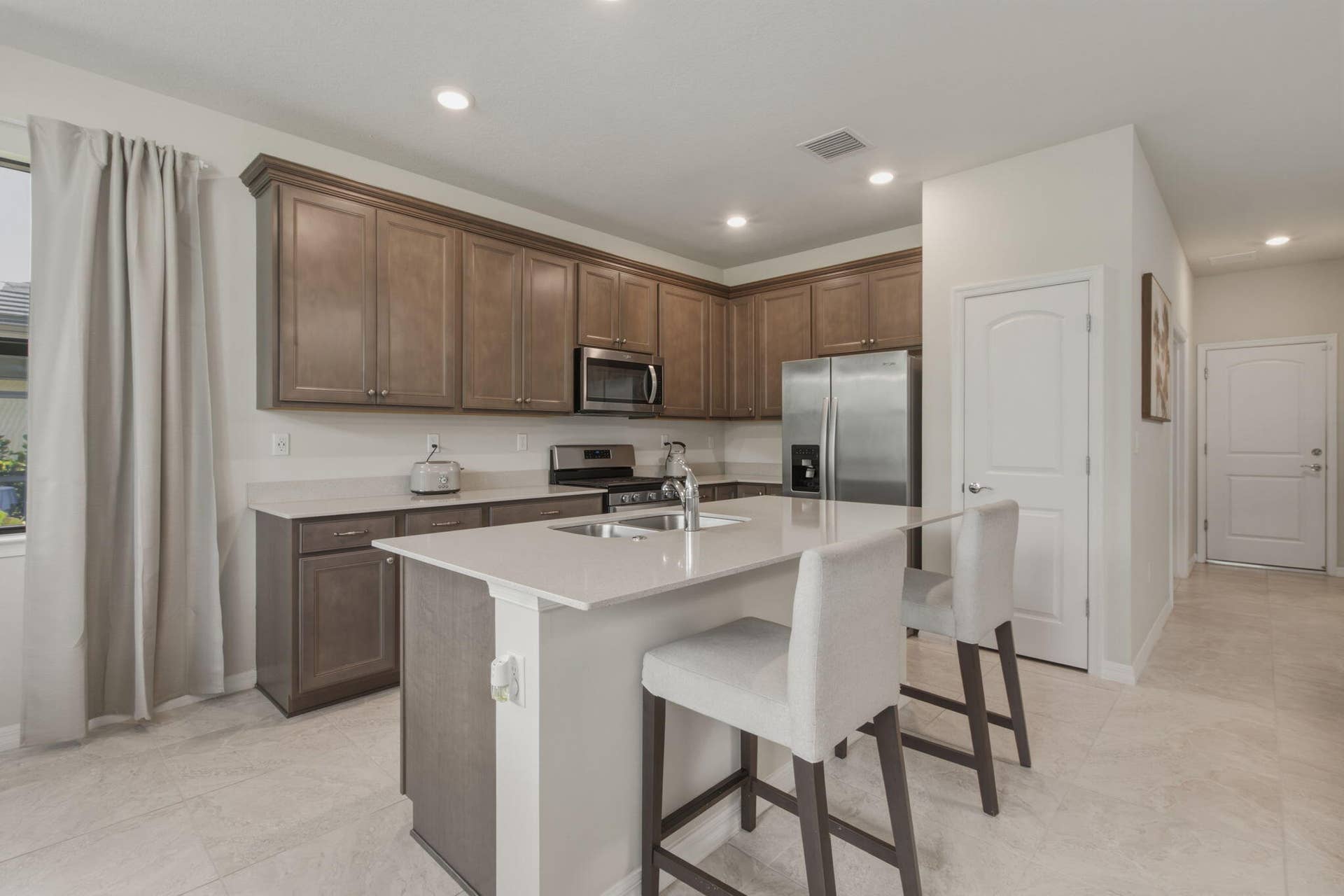 4601 Pinehurst Trail E, Oakland Park, FL 33309 Modern kitchen featuring wood-finish cabinetry, stainless steel appliances, and an island with an undermount sink
