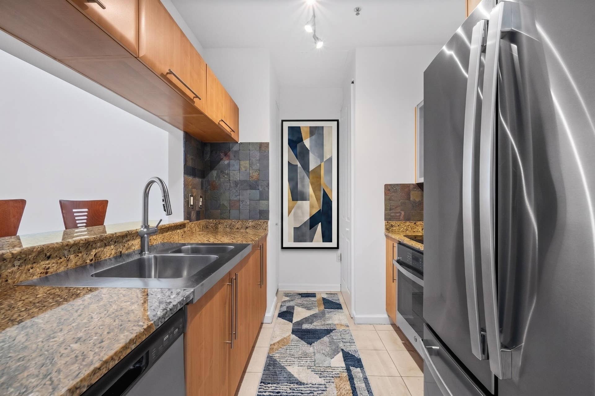 610 W Las Olas Boulevard, #115N, Fort Lauderdale, FL 33312 Well-appointed galley kitchen with granite countertops, warm-toned cabinetry, natural slate backsplash & newer stainless-steel appliances.
