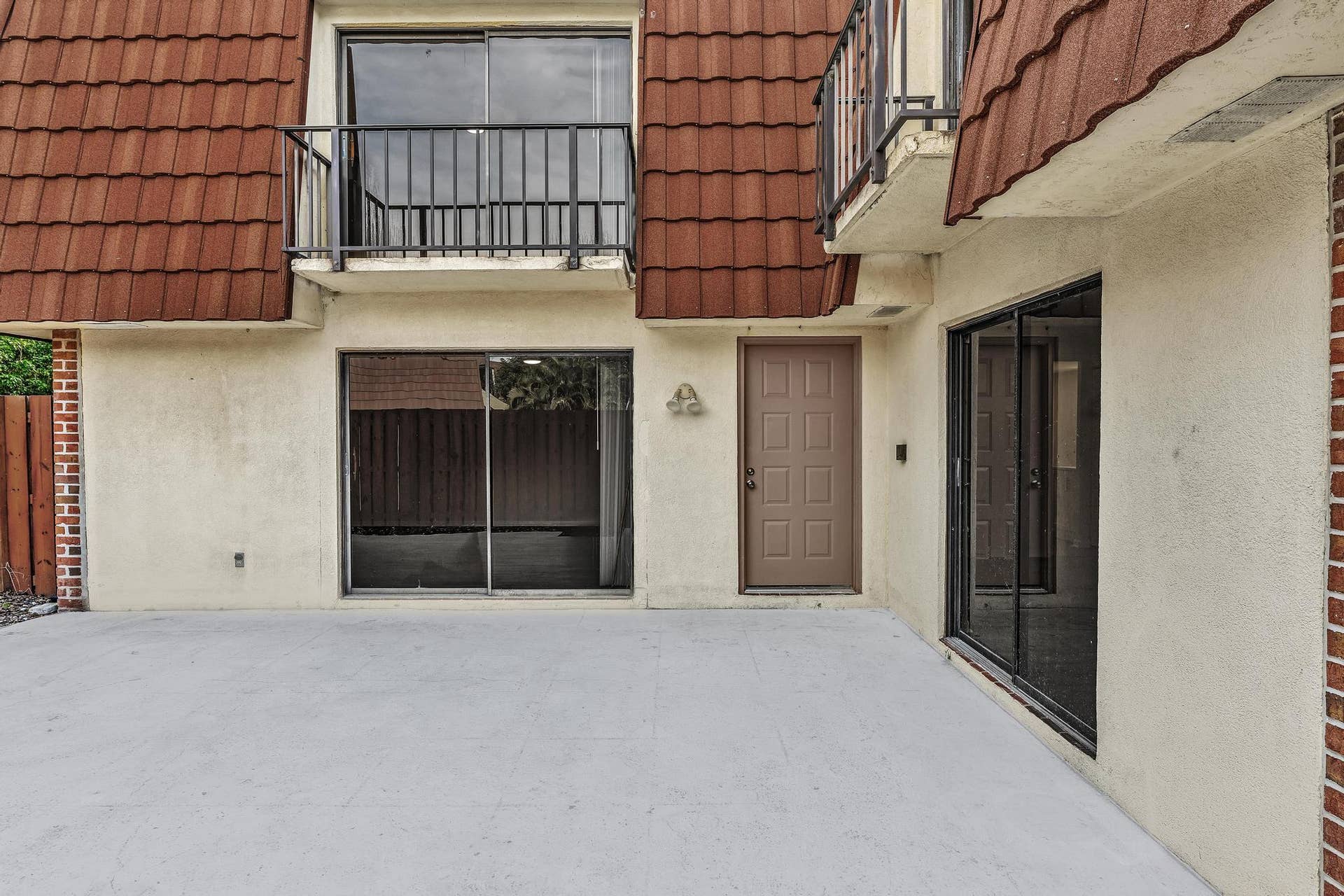 Exterior facade featuring a concrete patio, tile roofing, and multiple sliding glass doors